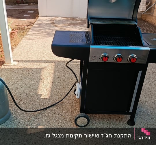 גריל גז חדש מחובר לבלון גז באמצעות צינור ווסת בחצר